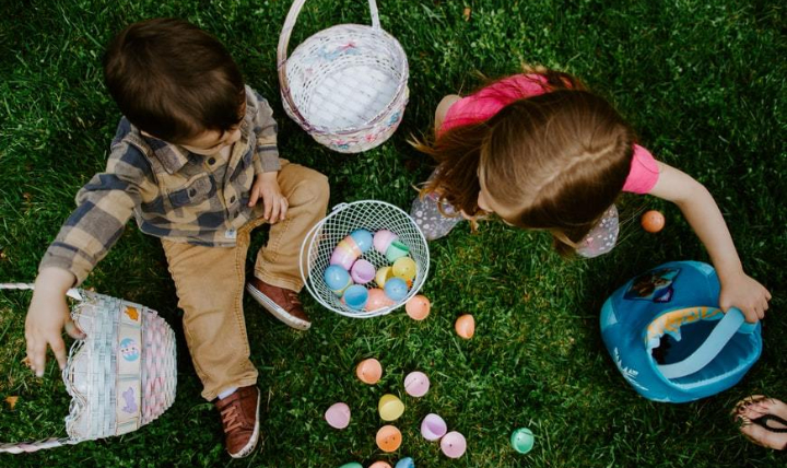 Two children sitting on some grass with Easter eggs and baskets.