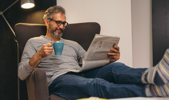 A man drinking a coffee at home with his feet up.