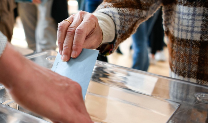 A person putting a ballot paper into a box.