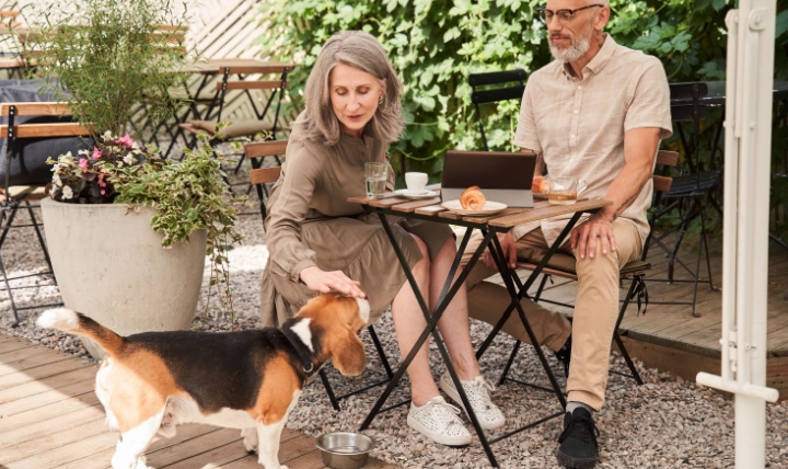 A couple sitting outside in a café with a dog.