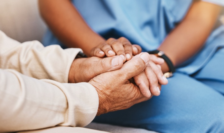 An elderly person holding hands with a nurse.