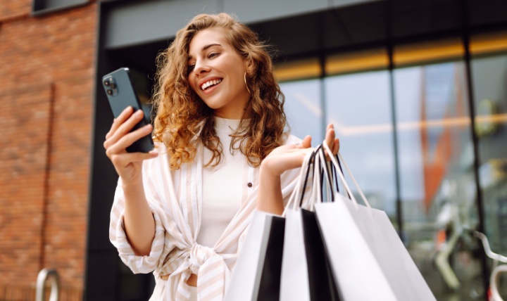 A woman holding shopping bags while on her phone.