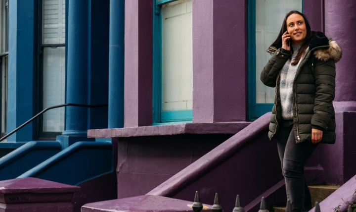 A woman walking out of a front door of a colourful row of terraced housing.