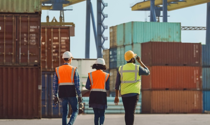 Workers walking through a shipping cargo container terminal depot.