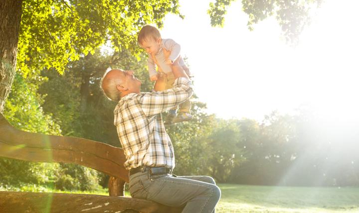 A grandfather playing with his young grandson in a park.