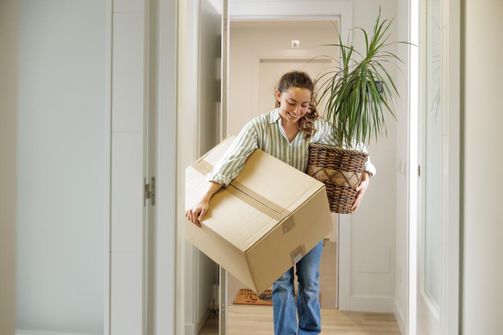 A woman carrying a box and a plant into her new home.