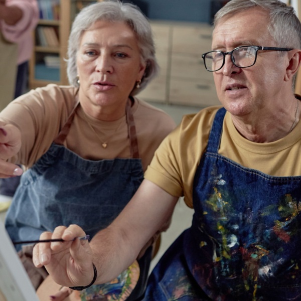 An older couple painting at an easel together.