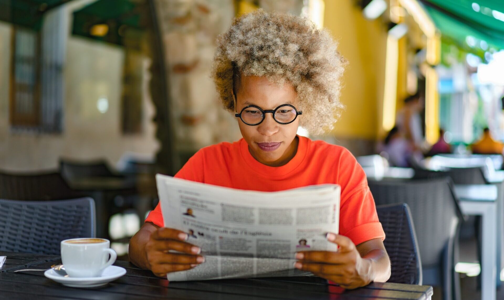 A woman reading a newspaper in a café.